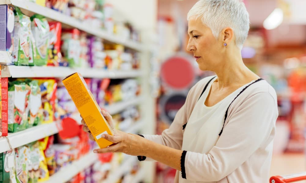 A woman reading the label on a box in a grocery store.