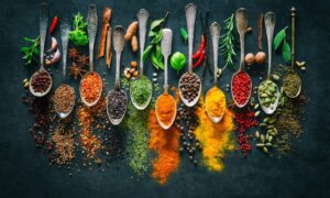 A photograph of various uncut, chopped, powdered spices sitting on spoons.
